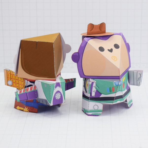 Paper toys of Woody and Buzz Lightyear from Toy Story. The image shows the characters have swapped accessories, now Buzz is wearing Woddy's hat and Woody is wearing Buzz's jetpack.