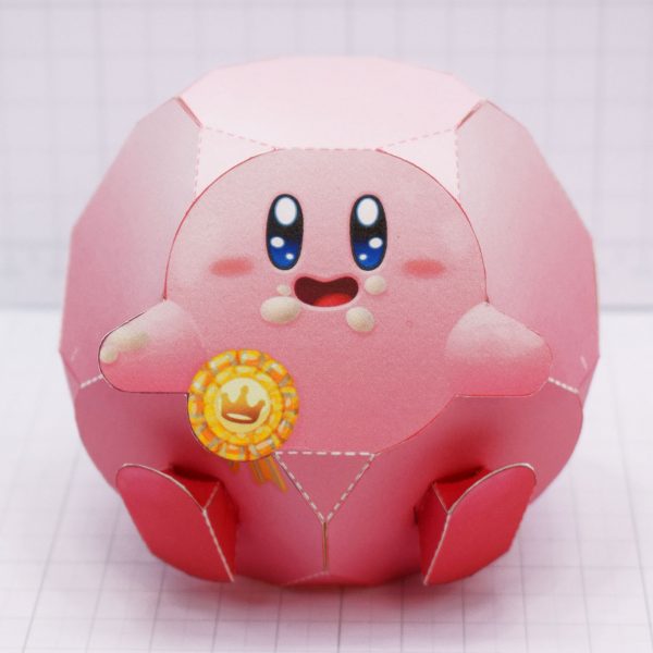 A photo of the Kirby's Dream Buffet paper toy once built, taken from the front , showing Kirby's smiling face and medal for coming in first place.