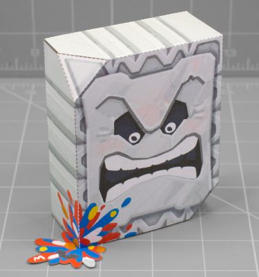 A photo of apapercraft depicting a Thromp from the Mario franchise, it's a big heavy rock block with an angry face. This photo is taken from the front