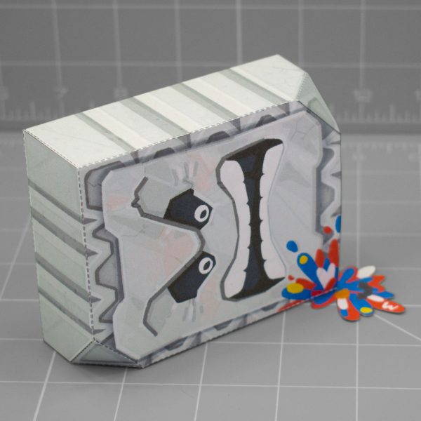 A photo of apapercraft depicting a Thromp from the Mario franchise, it's a big heavy rock block with an angry face. This photo is taken from on its side