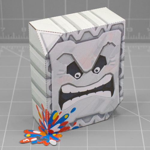 A photo of apapercraft depicting a Thromp from the Mario franchise, it's a big heavy rock block with an angry face. This photo is taken from the back