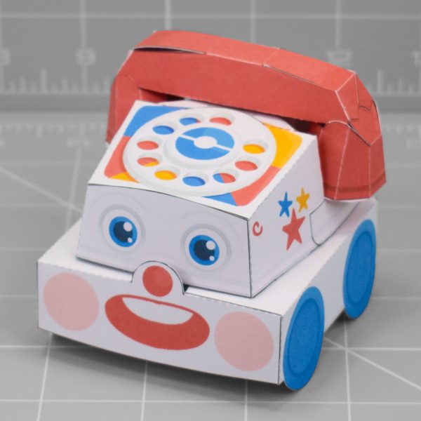 A photo of a papercraft depicting a retro children's toy phone. The papertoy has a cute face with an adorable smile.